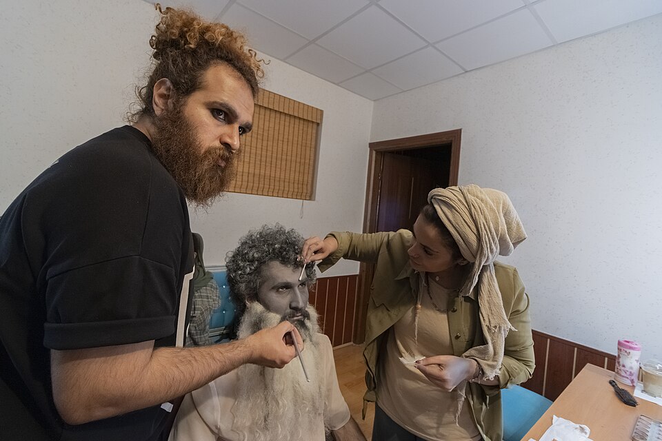 Δύο ιρανοί ψιμυθιολόγοι εν ώρα εργασίας στο καμαρίνι: με λεπτά πινέλα, επίθετη γενειάδα και γκρίζα περούκα μεταπλάθουν τον νεαρό ηθοποιό σε γέροντα. Η ψιμυθίωση γήρανσης συνιστά μία από τις απαιτητικότερες εφαρμογές της τέχνης τους.