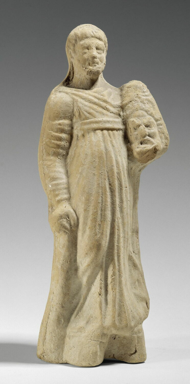 Πήλινο ειδώλιο τραγικού υποκριτή που υποδύεται τον Ηρακλή του [[#Ευριπίδη [Eurípides]#]]. Κρατάει προσωπείο και φοράει ποδήρη χιτώνα και κοθόρνους με υψηλές σόλες (175-150 π.Χ., Musée du Louvre, αρ. 1784).