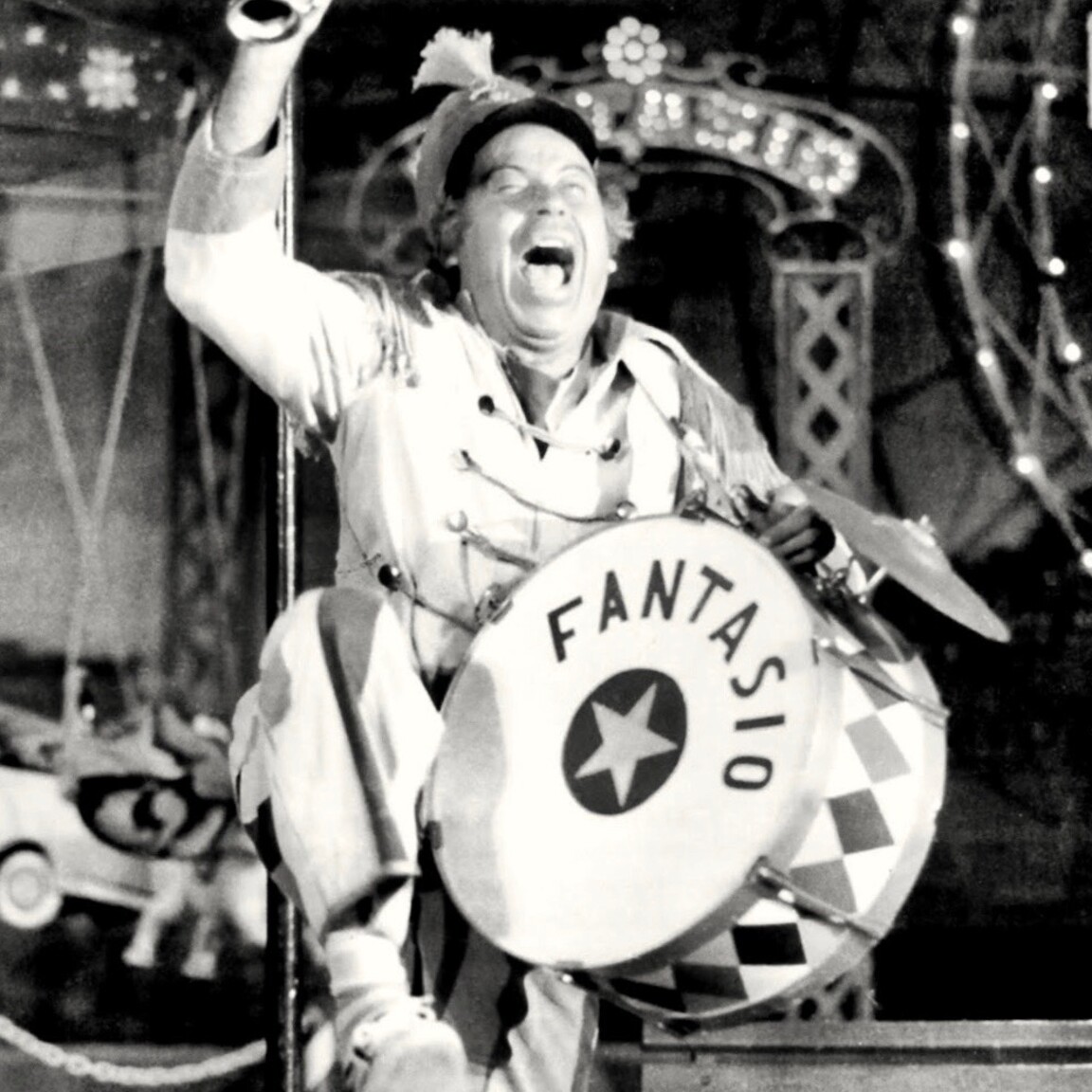 Φωτογραφικό στιγμιότυπο του [[#Θανάση Βέγγου#]], το οποίο αναδεικνύει την ιδιαίτερη κωμική του μανιέρα, από την παράσταση Ο τρελός του Λούνα Παρκ του [[#Γιώργου Λαζαρίδη#]] σε σκηνοθεσία [[#Κωστή Μιχαηλίδη#]]. Θέατρο Αμιράλ, θίασος Σμαρούλας Γιούλη, 1969. 