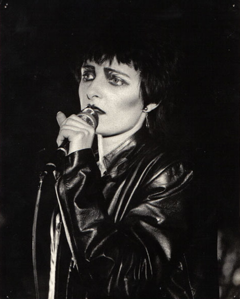 Η [[#Siouxsie Sioux [Σιούζι Σιού]#]], ηγετική μορφή του συγκροτήματος&nbsp;[[#Siouxsie and the Banshees#]], σε ζωντανή εμφάνιση στο Tiffany's του Εδιμβούργου το 1980. Η καλλιτέχνις αποτέλεσε κεντρικό πρόσωπο για τη διαμόρφωση της γοτθικής αισθητικής στη μουσική και τη μόδα, εισάγοντας ένα ιδιαίτερο οπτικό ύφος που βασίζεται στο έντονο μακιγιάρισμα και τη σκοτεινή ενδυμασία. Η συγκεκριμένη απεικόνιση καταγράφει τη μετάβαση από το ποστ-πανκ προς τη συγκρότηση της νεογοτθικής υποκουλτούρας, αναδεικνύοντας τη σημασία της σκηνικής παρουσίας στην ανάδειξη του ανοίκειου και του μυστηριώδους.
