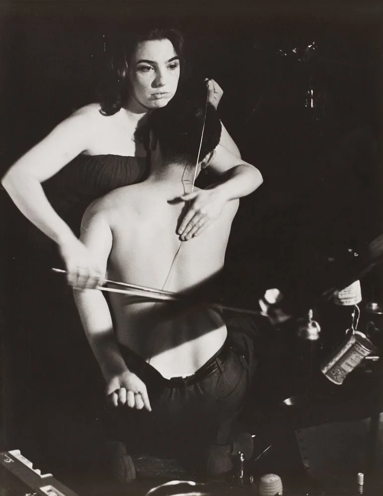 Φωτογραφία της επιτέλεσης των [[#Nam June Paik#]] [[#[Ναμ Τζουν Πάικ]#]] και [[#Charlotte Moorman#]] [[#[Σάρλοτ Μούρμαν]#]], John Cage's 26'1.1499" For a String Player,&nbsp;Νέα Υόρκη 1965. Στην επιτέλεση 26'1.1499" For a String Player, η μουσικός της πρωτοπορίας Charlotte Moorman και ο Nam June Paik (ένας από τους πιο επιδραστικούς καλλιτέχνες του Φλούξους  και της βιντεοτέχνης) ερμηνεύουν μια παρτιτούρα του [[#John Cage#]] [[# [Τζων Κέιτζ]#]], με την Moorman να κρατά το ημίγυμνο σώμα του Paik  σαν τσέλο, παίζοντας μια χορδή που είναι τεντωμένη στην πλάτη του. Έτσι τα σώματα των δύο καλλιτεχνών συνιστούν τόσο τα υποκείμενα που ενεργούν (Moorman) όσο και τα αντικείμενα πάνω στην οποία τελείται η ενέργεια της περφόρμανς (Paik). 