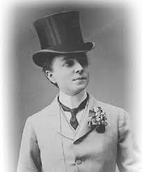 Η [[#Matilda Alice Powles [Ματίλντα Άλις Πάουλς]#]] (1864-1952) ως Vesta Tilley [Βέστα Τίλλεϋ], κορυφαία μιμήτρια ανδρών [male impersonator] των βρεττανικών μιούζικ χωλ. Η περσόνα του κομψού δανδή, με φράκο, ημίψηλο και μπαστούνι, συνιστά πρόδρομη μορφή του ντραγκ-κινγκ.