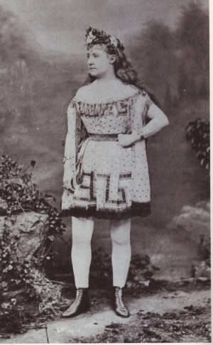 Η Lydia Thompson [Λύντια Τόμσον] ως Ιξίων, στο ομώνυμο μπουρλέσκ του Francis C. Burnand [Φράνσις Μπέρναντ]. Με τον ρόλο αυτό εμφανίστηκε για πρώτη φορά στη Νέα Υόρκη (1868), επικεφαλής του θιάσου British Blondes [Βρεττανίδες Ξανθές]. Ο δάφνινος στέφανος και ο μαίανδρος στο κοντό χιτώνιο παραπέμπουν στον μυθικό ήρωα, αλλά τα κολάν και τα ψηλά μποτάκια αναδεικνύουν το γυναικείο σώμα, που η ανδρική αμφίεση υποτίθεται ότι έκρυβε. Το βικτωριανό μπουρλέσκ δεν έκρυβε την απόσταση ανάμεσα στο κοινωνικό φύλο του ρόλου και στο σώμα της ερμηνεύτριας· την αξιοποιούσε για σάτιρα και ερωτική γοητεία.