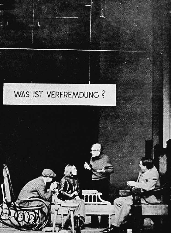 «Τι είναι ανοικείωση;»: Στιγμιότυπο από τη σκηνική παρουσίαση/συζήτηση, το 1963, του θεωρητικού έργου του Brecht, Διάλογοι για την αγορά του χαλκού [The Messingkauf Dialogues/Dialoge aus dem Messingkauf, (1939 -1942)],&nbsp;γραμμένο υπό μορφή κριτικού διάλογου για το θέατρο, στο Berliner Ensemble, όπου διακρίνονται οι παρουσιαστές - συνομιλητές σε αντίστοιχους «ρόλους» μέσα από το έργο: (από αριστερά) ο [[#Ekkehard Schall [Έκεχαρτ Σαλ]#]] ως ο Φιλόσοφος, η [[#Gisela May [Γκίζελα Μέι]#]], ως η Ηθοποιός, ο [[#Willy Schwabe [Βίλι Σβάμπε]#]] ως ο Δραματουργός και ο [[#Wolf Kaiser [Βολφ Κάιζερ]#]] ως ο Ηθοποιός. Στους Διαλόγους για την αγορά του χαλκού, ο Brecht παρουσιάζει την θεατρική θεωρία του και για την ανοικείωση, εξηγώντας πως ο ηθοποιός, ο σκηνοθέτης, η μουσική και τα σκηνικά συμβάλλουν στο να μη βυθιστεί το κοινό στην ψευδαίσθηση αλλά να δει κριτικά την πραγματικότητα.