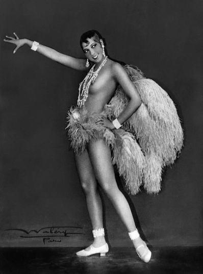 Η Joséphine Baker [Ζοζεφίν Μπαικέρ] (1906-1975) σε εμβληματική φωτογράφιση του στούντιο Waléry [Βαλερύ] των Παρισίων (περ. 1926), με κοστούμι από φτερά στρουθοκαμήλου, μαργαριταρένια κοσμήματα και λευκές γόβες, σε χορευτική στάση θριάμβου. Η Αφροαμερικανή ερμηνεύτρια, εμβληματική φιγούρα της Jazz Age, καθιέρωσε το γυμνό (ή ημίγυμνο) σκηνικό σώμα ως κεντρικό εκφραστικό μέσο της παρισινής επιθεώρησης του Μεσοπολέμου στις παραστάσεις της στα Folies Bergère [Φολί Μπερζέρ].
