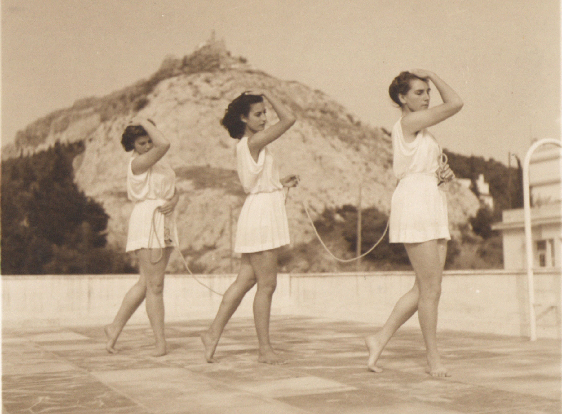 Οι μαθήτριες της Κούλας Πράτσικα προγυμνάζονται στην ταράτσα του σπιτιού της, στο οποίο στεγάστηκε η σχολή της, νυν Κρατική Σχολή Χορού / ΚΣΟΤ. Αρχείο [[#Πέλου Κατσέλη#]] και [[#Αλέκας Κατσέλη#]], ΕΛΙΑ/ΜΙΕΤ.]. 