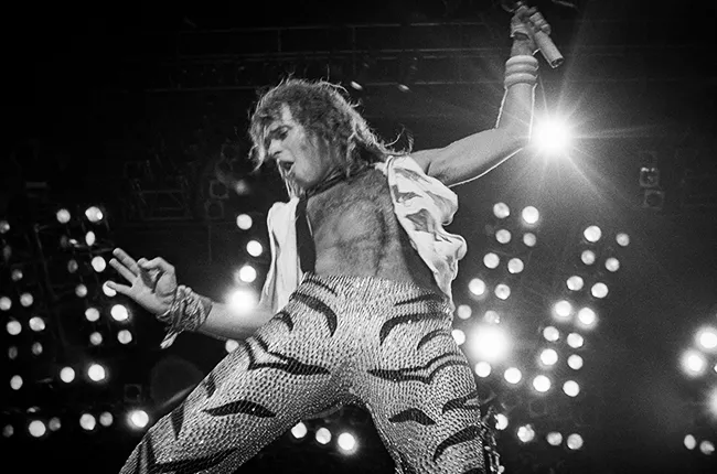 Ο [[#David Lee Roth [Ντέιβιντ Λη Ροθ]#]], ιστορικός επικεφαλής τραγουδιστής των [[#Van Halen [Βαν Άλεν]#]], κατά τη διάρκεια συναυλίας. Με τη σπινθηροβόλο σκηνική του παρουσία, τα ακροβατικά άλματα, την υπερβολική σωματική ενέργεια και τη χαρισματική επικοινωνία με το κοινό, ο Roth ενσάρκωσε παραδειγματικά τη «θηριώδη ομορφιά» και τη διονυσιακή θεατρικότητα του κεντρικού τραγουδιστή της χέβυ μέταλ, καθιερώνοντας ένα πρότυπο σκηνικής επιτέλεσης που συνδύασε το glam, την αθλητική ευρωστία και τη χιουμοριστική αυτοαναφορικότητα.