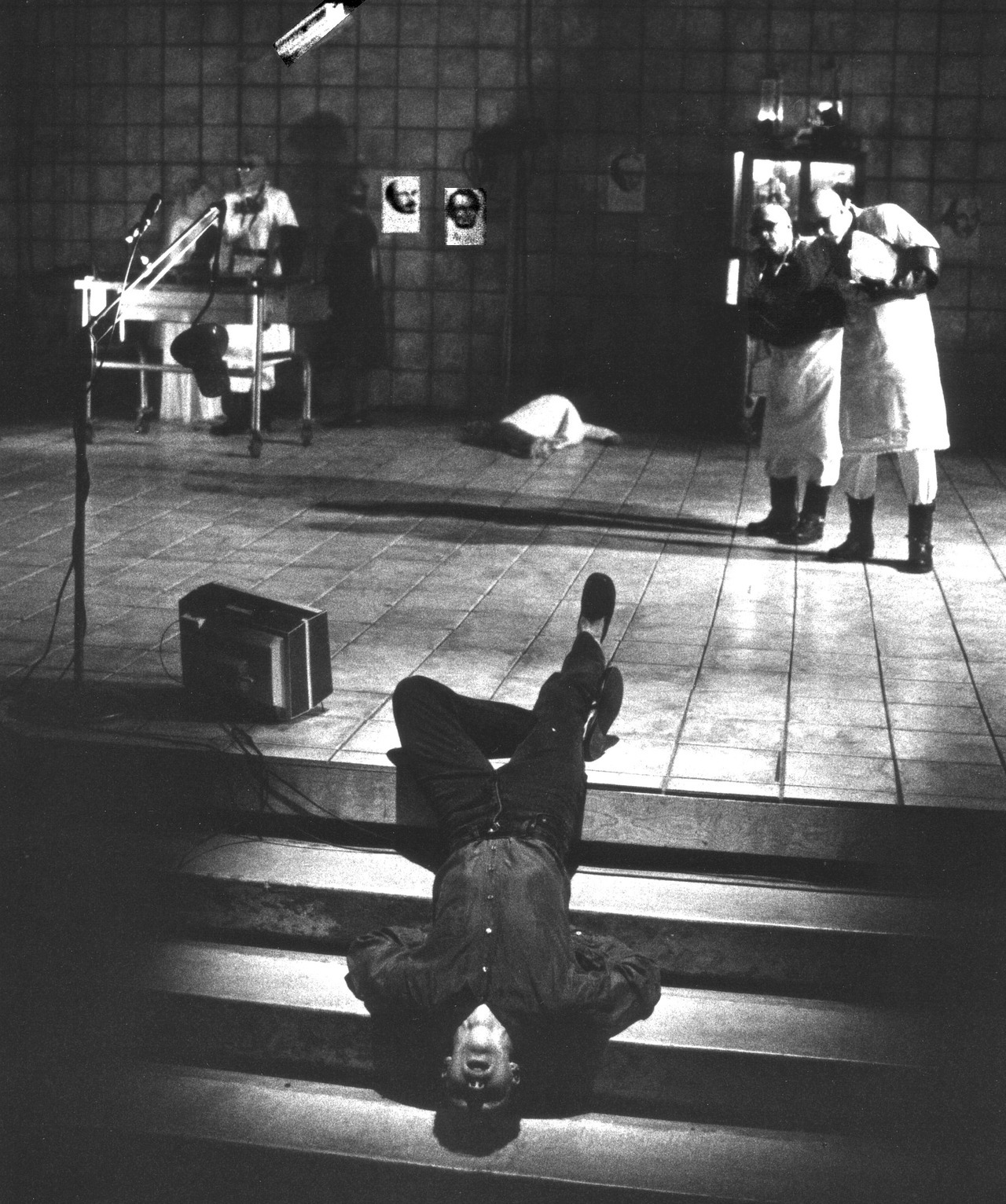 Σκηνή από το Die Hamletmaschine [Η Αμλετομηχανή] του Heiner Müller, University of California, Irvine, 1992. Η αποδόμηση του σαιξπηρικού Hamlet [Άμλετ] μεταφέρεται στη σκηνή ως διάλυση του δραματικού χαρακτήρα και του σκηνικού χώρου: το σώμα του ερμηνευτή εκτίθεται ανάστροφο, οι μορφές διασπείρονται σε ασύνδετες εστίες δράσης και τα εικονογραφικά θραύσματα λειτουργούν ως υπολείμματα μιας αφήγησης που έχει καταλυθεί.