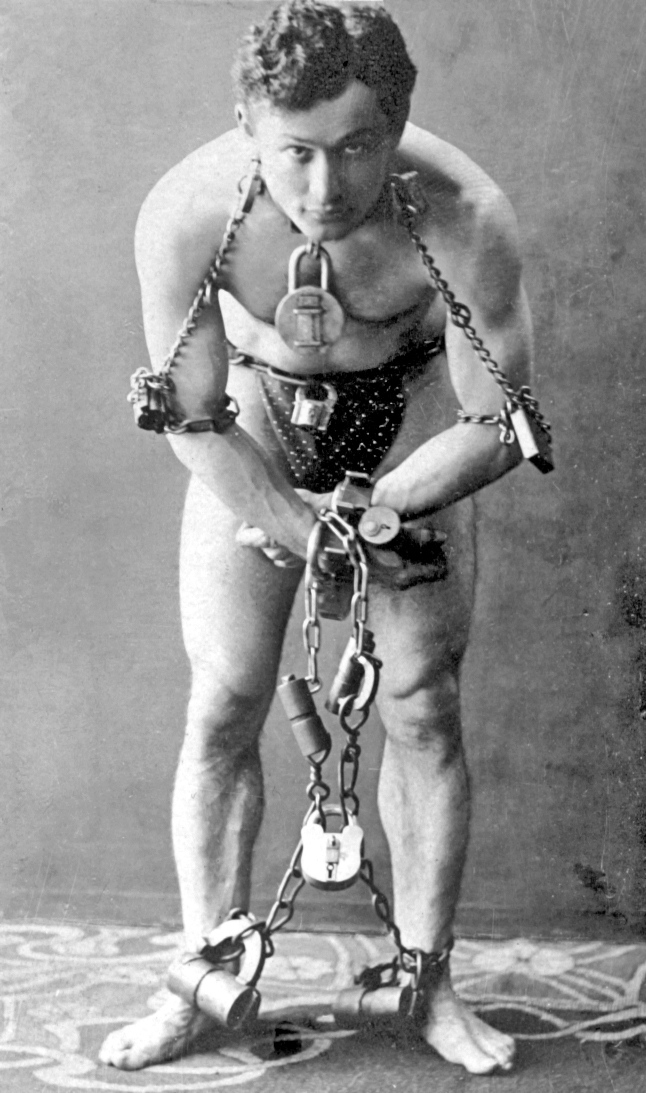 Ο Harry Houdini [Χάρρυ Χουντίνι], ολόσωμος και αλυσοδεμένος, σε φωτογραφία περ. 1899. Η δημόσια περσόνα του, η τεχνική δεξιότητα και η συστηματική προβολή των αποδράσεών του τον καθιέρωσαν ως έναν από τους χαρακτηριστικότερους σόου μαν της διεθνούς ψυχαγωγίας των αρχών του 20ού αιώνα. 
