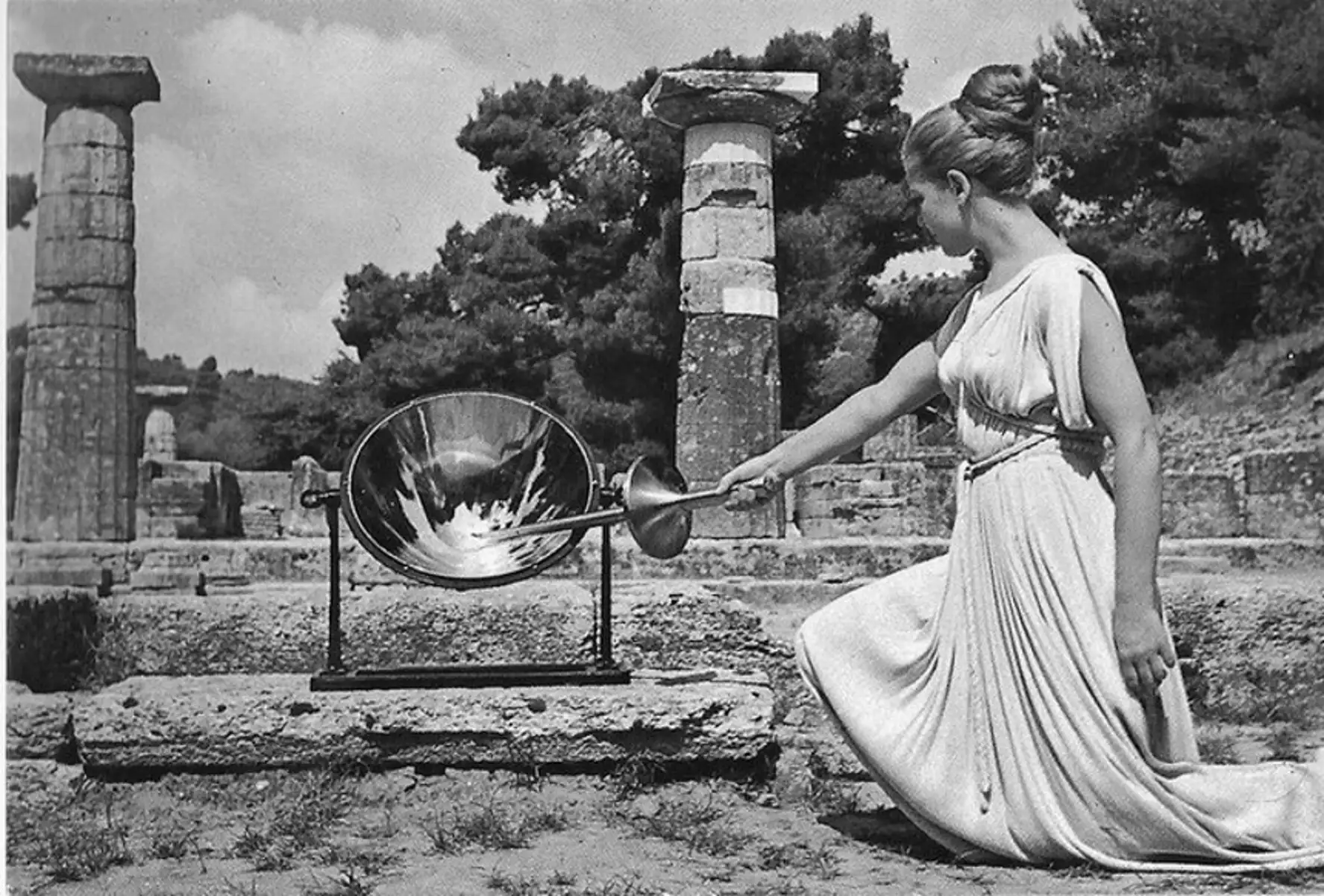 Η Μαρία Μοσχολιού ως Πρωθιέρεια στην τελετή Αφής της Ολυμπιακής Φλόγας στην Αρχαία Ολυμπία, ρόλο που επιτέλεσε σε τέσσερις Ολυμπιάδες (1968, 1972, 1976, 1980). Η ηθοποιός του Εθνικού Θεάτρου, με χορογραφία Μαρίας Χορς, ενσάρκωσε μια επινοημένη ιερατική μορφή: η σύγχρονη τελετή δανείζεται από την αρχαιότητα τη σκευή, τη χειρονομία και τον στυλιζαρισμένο βηματισμό για να νομιμοποιήσει έναν διεθνή θεσμό.