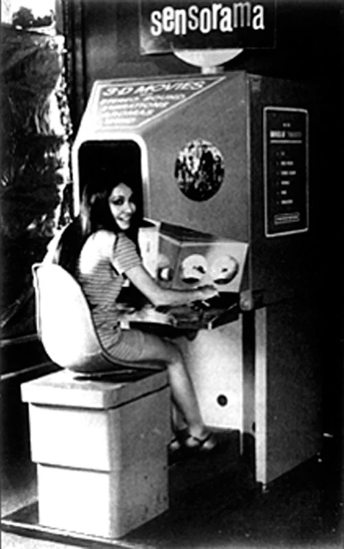 Το Sensorama (1962) του Morton Heilig [Μόρτον Χάιλιγκ], ατομικό μηχάνημα θέασης με στερεοσκοπική εικόνα, στερεοφωνικό ήχο, δονήσεις, ρεύματα αέρα και οσμές. Θεωρείται πρόδρομος της εικονικής πραγματικότητας, καθώς επεδίωξε πρώτο τη συνολική αισθητηριακή εμβύθιση του/της θεατή/θεάτριας.