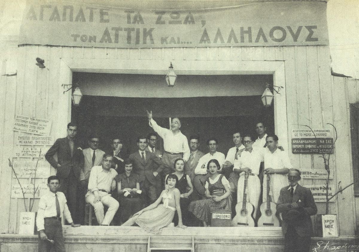 Ο θίασος της «Μάντρας» του Αττίκ (όρθιος στο μέσον) επί σκηνής, σε φωτογραφία του 1931, με φόντο το σύνθημα «Αγαπάτε τα ζώα, τον Αττίκ και... αλλήλους». 